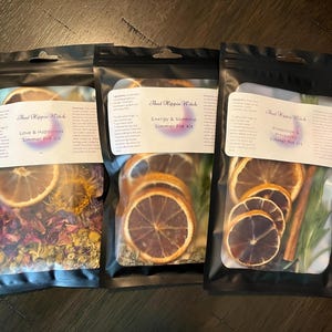 Peut inclure: Trois sachets noirs avec des étiquettes blanches qui indiquent "That Hippie Witch" et contiennent différents kits de pots mijotés. Les étiquettes indiquent également les parfums de chaque kit : "Love & Happiness", "Energy & Stamina" et "Protection & Prosperity".