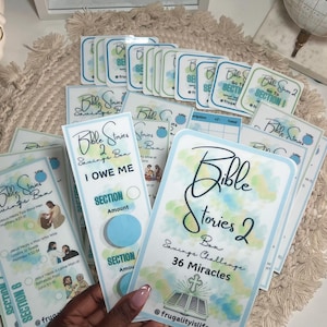 May include: A collection of Bible Stories 2 Savings Box cards and bookmarks. The cards have a watercolor design with blue and green accents. The text includes "Bible Stories 2 Box Savings Challenge 36 Miracles".