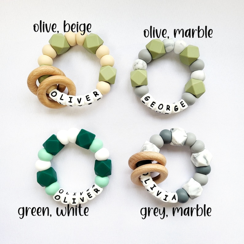 May include: Four silicone teething rings with wooden rings and personalized names. The rings are in different color combinations: olive and beige, olive and marble, green and white, and grey and marble.