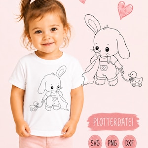 Könnte beinhalten: Ein weißes T-Shirt mit einer schwarzen Strichzeichnung eines Hasen in Latzhose, der eine Decke hält und eine Spielzeugente auf Rädern zieht. Das Design enthält kleine handgezeichnete Herzen und den Text PLOTTERDATEI mit SVG, PNG und DXF Labels.