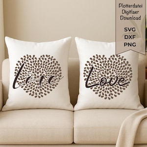 Può includere: Due cuscini bianchi con un design a forma di cuore marrone composto da piccole forme di foglie. La parola "love" è scritta in corsivo sul cuore. I cuscini sono su un divano beige.