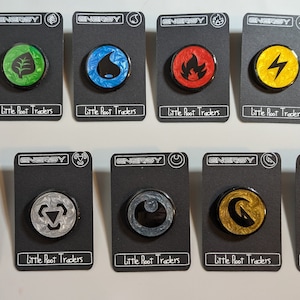 Puede incluir: Diez cartas de energía Pokémon diferentes con varios colores y diseños. Cada carta tiene la palabra "ENERGY" en la parte superior y "Little Root Traders" en la parte inferior.