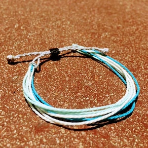 May include: A multi-colored string bracelet with blue, white, and light blue strands. The bracelet has a black clasp.