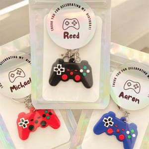 May include: Keychains shaped like game controllers in red, black, and blue. Each keychain has a different name on a circular tag that says "Thank you for celebrating my birthday!" The controllers have colorful buttons.