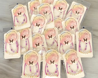 May include: A collection of personalized necklaces, each packaged on a white card with a clear plastic sleeve. The necklaces feature white letter beads spelling out names, with purple and gold accent beads. Each package has a circular sticker with text.