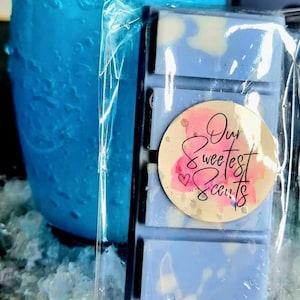 May include: A blue wax melt bar with a white swirl design. The bar has a round sticker with the text "Our Sweetest Scents" in pink and white lettering.