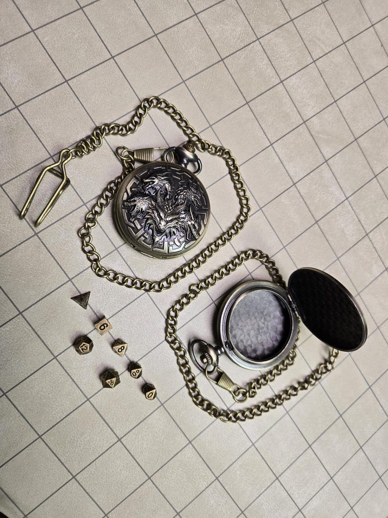 May include: A silver pocket watch with a detailed dragon design on the cover, attached to a chain. Beside it are several dice, including a D20, D12, D8, D6, and D4, all in a bronze color. The watch is open, revealing the inside.