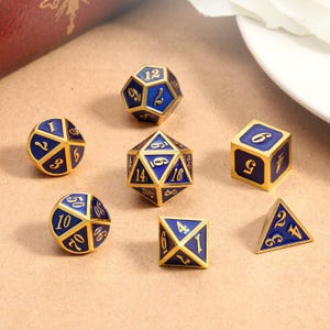 Op de afbeelding: Een set van zeven polyhedrale dobbelstenen in goud en blauw. De dobbelstenen bevatten een d4, d6, d8, d10, d12, d20 en een percentagedobbelsteen. Elke dobbelsteen heeft gouden randen en blauwe vlakken met gouden cijfers.