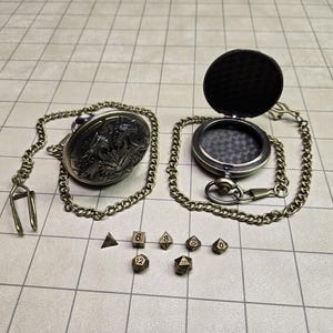 May include: An antique-style pocket watch with an open lid, chain, and a set of polyhedral dice. The watch has a detailed floral design on the back. The dice are in various shapes and sizes, perfect for tabletop gaming.