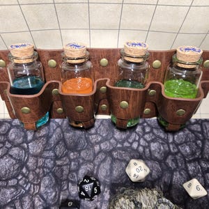 May include: A brown leather potion holder with four glass bottles filled with blue, orange, green, and green liquids. The holder has brass rivets and is sitting on a grey stone-patterned surface.