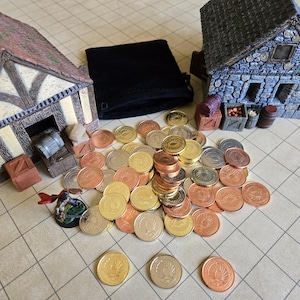 Puede incluir: Una escena de mesa con edificios en miniatura, una bolsa de terciopelo negro y una colecci&oacute;n de monedas doradas, plateadas y cobrizas. Los edificios tienen detalles arquitect&oacute;nicos y las monedas est&aacute;n dispersas.