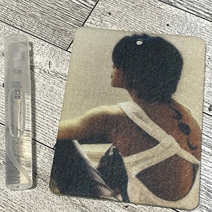 May include: A white ceramic car air freshener with a photo of a woman with short black hair. The woman is wearing a white tank top and has a tattoo on her back.