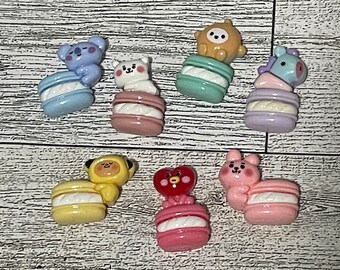 May include: A set of seven colorful macaron charms featuring various cartoon characters. Each charm is made of polymer clay and features a different character, including a bear, a unicorn, a bunny, a pig, a chick, and a heart. The charms are perfect for adding a touch of whimsy to your jewelry, bags, or other accessories.