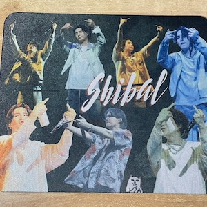 Könnte beinhalten: Ein farbenfrohes Mauspad mit einer Gruppe von Menschen, die ihre Hände in die Luft strecken. Das Wort "Shibal" ist in weißen Kursivbuchstaben über das Bild geschrieben.