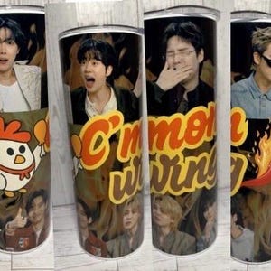 Op de afbeelding: Een cilindrische roestvrijstalen beker met een collage van vier afzonderlijke foto's van K-pop-groepsleden, een cartoonkip die drumsticks vasthoudt, een rode chilipeper en de gele tekst C'mon wings op een zwarte achtergrond.