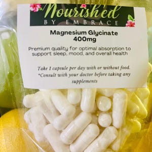 May include: A white plastic bag filled with white capsules labeled "Nourished by Embrace Magnesium Glycinate 400mg". The label also includes the text "Premium quality for optimal absorption to support sleep, mood, and overall health. Take 1 capsule per day with or without food. *Consult with your doctor before taking any supplements."