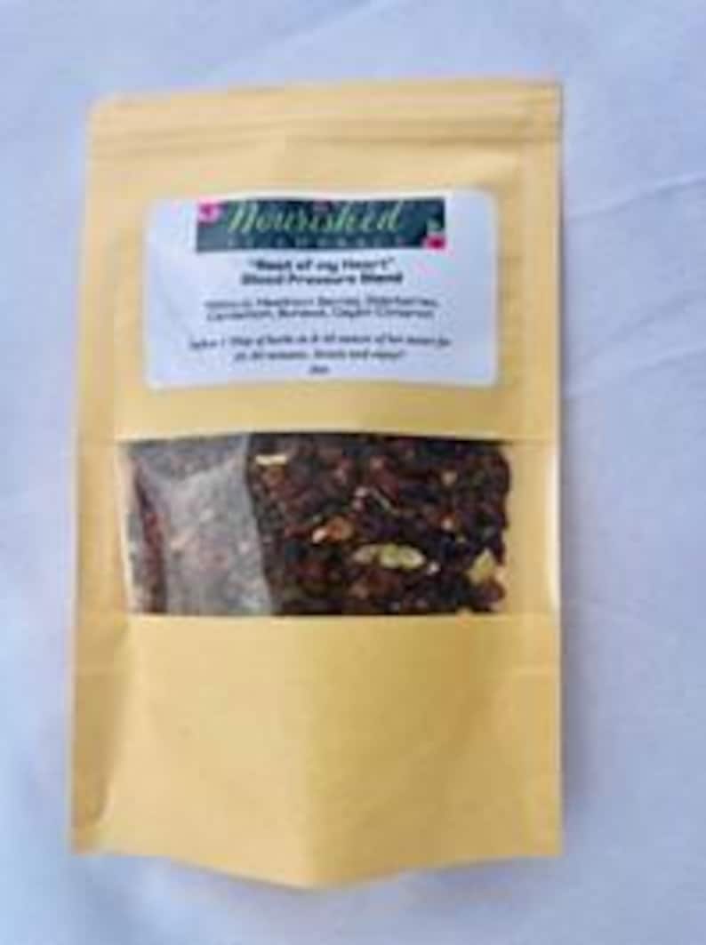 Pu&ograve; includere: Un sacchetto di carta marrone con una finestra trasparente che mostra un mix di erbe e spezie essiccate. Il sacchetto ha un'etichetta che recita "Nourished Naturals" e "'Beat of my Heart' Blood Pressure Blend".