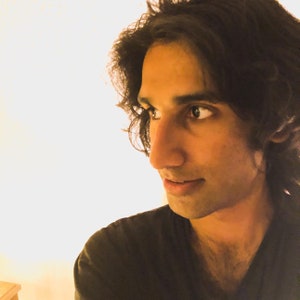 May include: A close-up portrait of a person with long, dark brown hair. The person is wearing a black shirt and looking to the right.