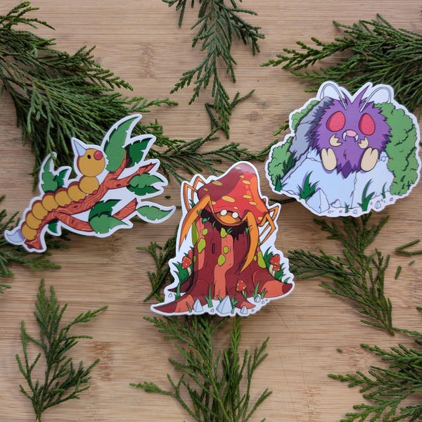 May include: Three cartoon stickers featuring a yellow and orange worm on a branch, a red and orange mushroom with a spider, and a purple creature with a red face on a rock.