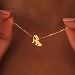 May include: A gold chain necklace with a pendant shaped like a dog sitting and holding a leash in its mouth.