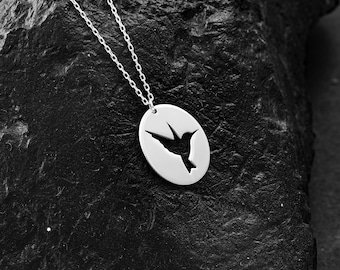 May include: A silver necklace with a round pendant featuring a cut-out hummingbird silhouette.