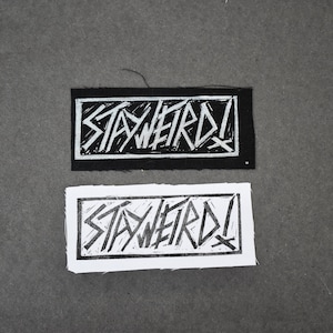 Puede incluir: Dos parches de tela con las palabras "STAY WEIRD!" impresas en blanco sobre fondo negro y negro sobre fondo blanco.