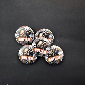 May include: Five circular badges featuring a skull design and the word "AUTISM" in red and white. The badges are set against a black background and have a shiny surface.