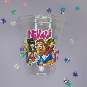 May include: Clear plastic cup with a pink and purple sticker featuring a group of cartoon girls with the name "Nikki" printed on the sticker.