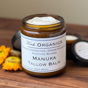 May include: A jar of Manuka Tallow Balm from Kersh Organics, with a white label and a black lid. The jar is filled with a white cream and is surrounded by yellow flowers. The text on the label reads "Manuka Tallow Balm".