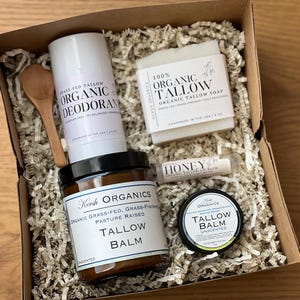 May include: A gift box filled with organic skincare products. Includes a deodorant stick, a jar of tallow balm, a bar of tallow soap, a lip balm, and a small jar of unscented tallow balm. The products are nestled in paper filler.