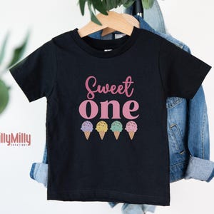 May include: Black t-shirt with the text "Sweet One" in pink lettering and a row of three colorful ice cream cones below.