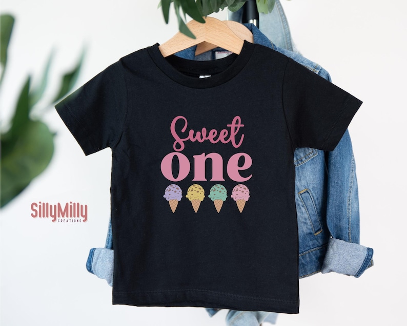 May include: Black t-shirt with the text "Sweet One" in pink lettering and a row of three colorful ice cream cones below.