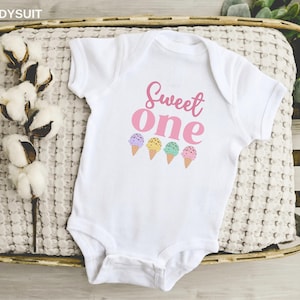 May include: White baby onesie with the text "Sweet One" in pink lettering and four colorful ice cream cones printed on the front.