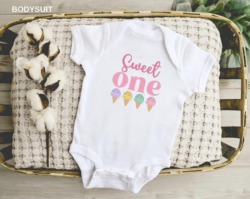 May include: White baby onesie with the text "Sweet One" in pink lettering and four colorful ice cream cones printed on the front.