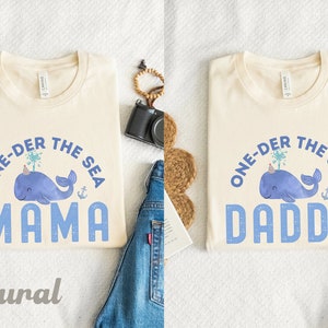May include: Two cream colored t-shirts with a blue whale graphic and the text "One-der the Sea" with the words "Mama" and "Daddy" below the whale.