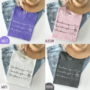 May include: Four t-shirts in different colours, violet, pink, white, and grey, with the text "Gardening Sourdough Chickens" and a graphic of a loaf of bread and two chickens.