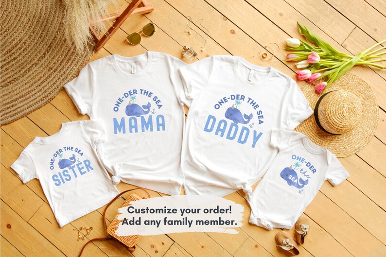May include: A set of four white t-shirts with a blue whale graphic and the text "One-der the Sea" with a different word for each shirt: "Mama", "Daddy", "Sister", and "the Sea".