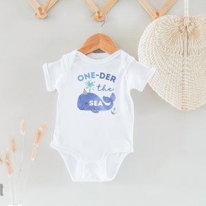 May include: White baby bodysuit with a blue whale graphic and the text "ONE-DER the SEA".