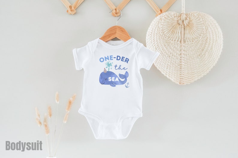 May include: White baby bodysuit with a blue whale graphic and the text "ONE-DER the SEA".