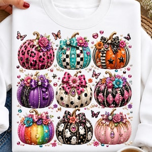 May include: A white crewneck sweatshirt featuring a graphic print of nine decorative pumpkins. The pumpkins are adorned with various patterns including leopard print, polka dots, stripes, and ghosts, accented with colourful bows, flowers, and pearls.