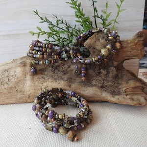 May include: Two multi-strand wrap bracelets featuring a collection of purple, brown, and metallic beads. The bracelets are constructed with various textures, including faceted, smooth, and patterned beads, accented with small bronze-toned metal charms.