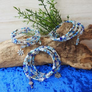 May include: Three spiral wrap bracelets featuring a mix of blue, white, and clear glass beads on silver-toned wire. Each bracelet is accented with small silver-colored snowflake charms, creating a cohesive set of winter-themed jewelry pieces.
