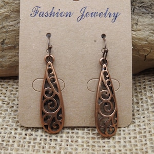 May include: A pair of copper-colored teardrop earrings with an open filigree design. The earrings are displayed on a brown card with the words "Fashion Jewelry" in cursive script.