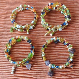 May include: Four multi-strand wrap bracelets featuring an assortment of colorful glass beads in shades of green, blue, orange, yellow, and white. Each bracelet includes small metallic accents and dangling leaf-shaped charms in various colors.