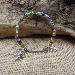 May include: A silver-toned bracelet with colorful beads and charms. The bracelet features a series of small, multi-colored beads in a rainbow pattern. Two charms dangle from the bracelet: a figure and a heart.