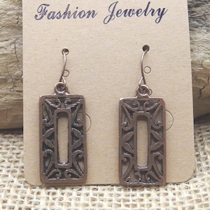 May include: A pair of copper-colored rectangular earrings with an openwork design. The earrings are displayed on a brown card with the words "Fashion Jewelry" printed at the top. The earrings have a hook closure.