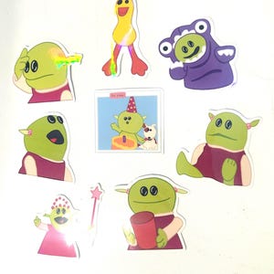 May include: A collection of colorful stickers featuring cartoon characters. The stickers depict various green-skinned creatures in different poses and outfits, including a frog costume, a birthday scene, and holding a red cup. The stickers are on a white background.