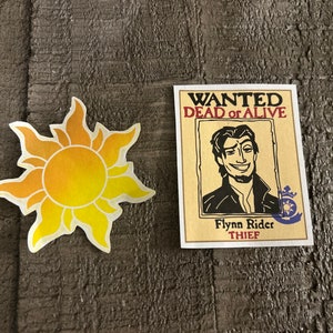 K&ouml;nnte beinhalten: Ein Fahndungsplakat mit einer Cartoon-Illustration von Flynn Rider, einem Dieb, mit dem Text "WANTED DEAD or ALIVE" und "Flynn Rider THIEF". Das Plakat befindet sich neben einer gelben Sonne mit Strahlen.