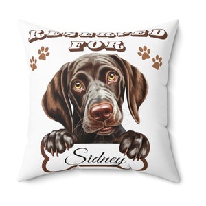 May include: White pillow with a brown and black German Shorthaired Pointer dog peeking over a bone-shaped sign that says "Reserved for Sidney".