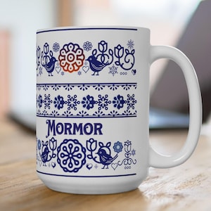 May include: White ceramic mug with a blue and white Scandinavian-inspired pattern featuring birds, flowers, and snowflakes. The word "MORMOR" is printed in blue on the mug.